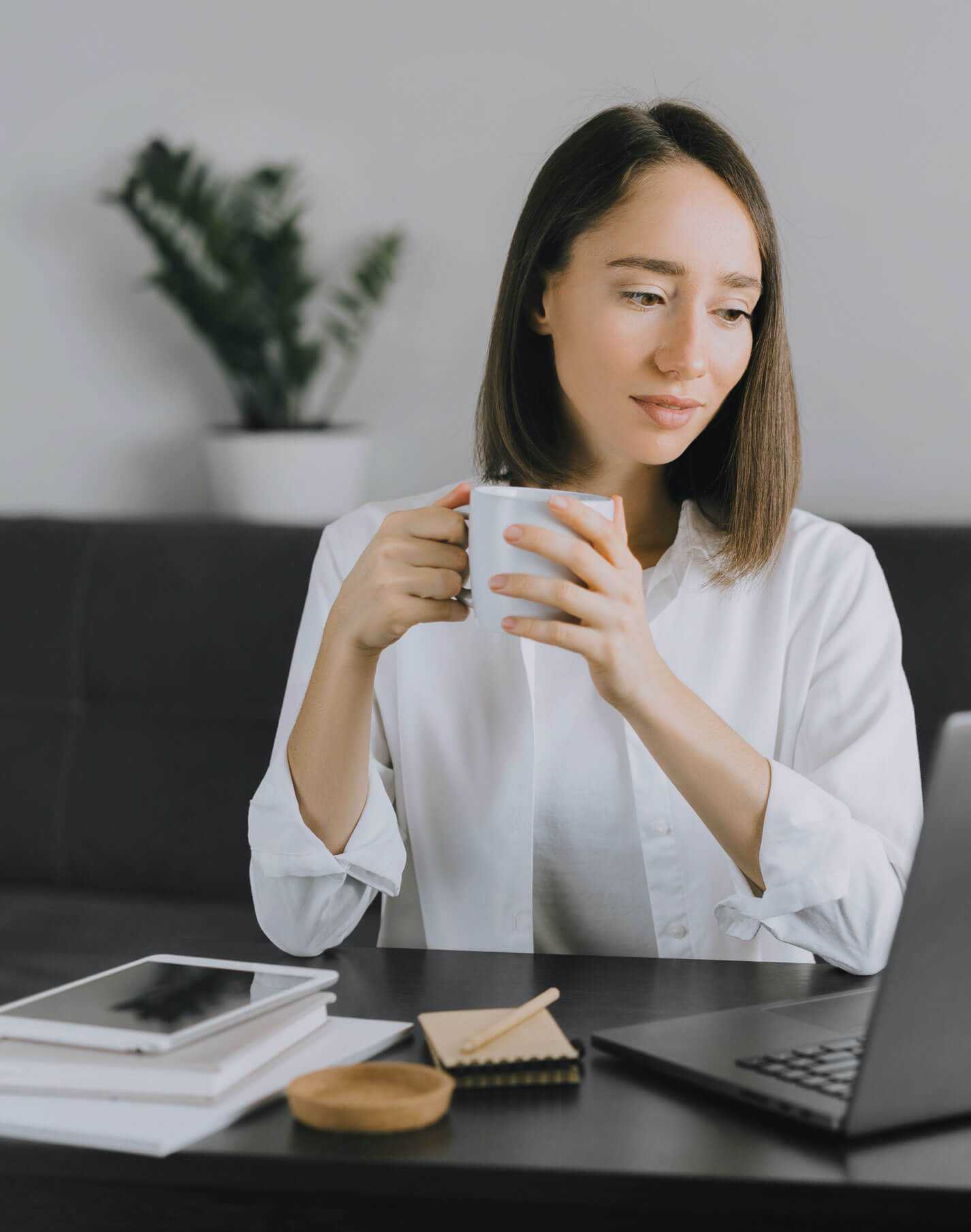 Een vrouw drinkt koffie en checkt haar cv-website op een laptop.