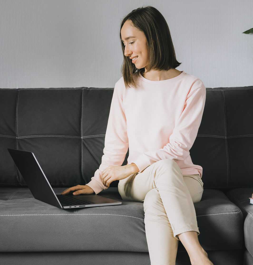 Eine Frau sitzt auf ihrer Couch und arbeitet an ihrem Laptop an ihrer Bewerbungshomepage.